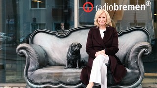 Maren Kroymann sitzt auf dem Loriotsofa, das direkt am Eingang von Radio Bremen steht.