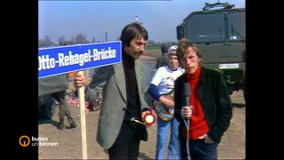 Die Moderatoren Michael Geyer und Christian Berg stehen vor einer Brücke