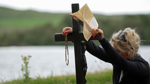 Eine Pilgerin lehnt an ein Holzkreuz in Irland